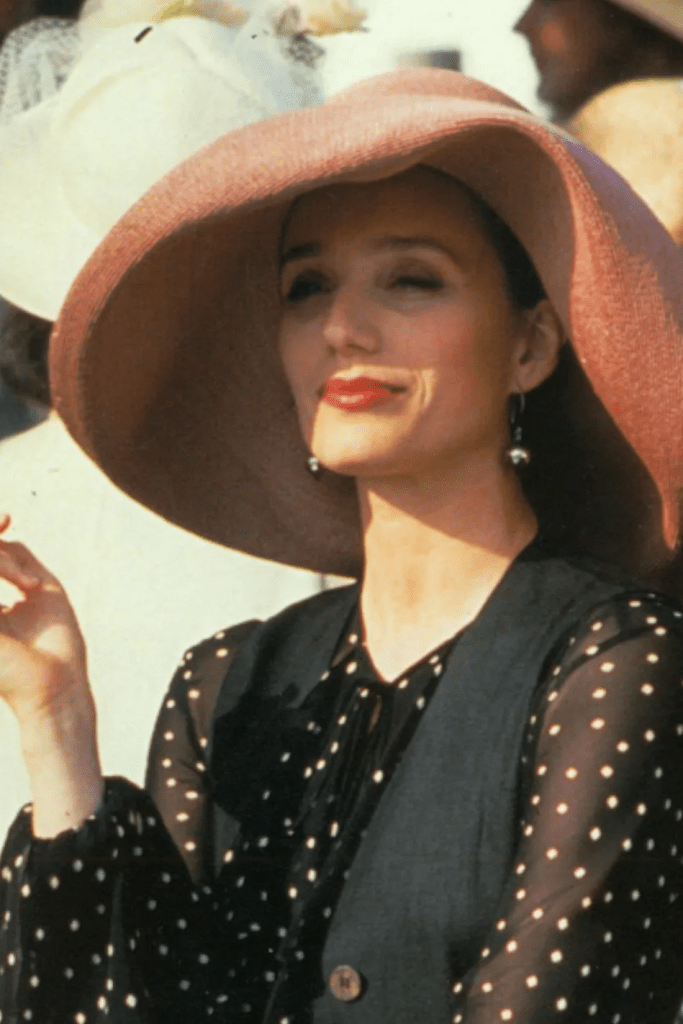 Kristin Scott Thomas as Fiona in “Four Weddings and a Funeral” (1994) wearing a large, floppy pink hat and formal attire.