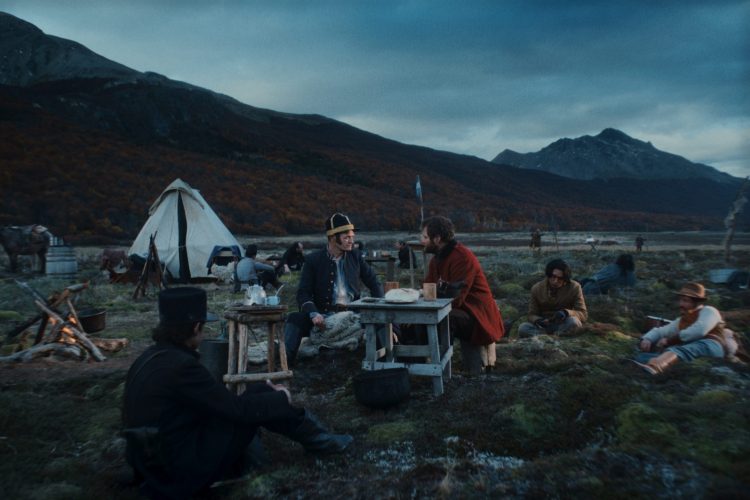A British soldier and American mercenary sit at a campsite against a rugged Patagonian backdrop