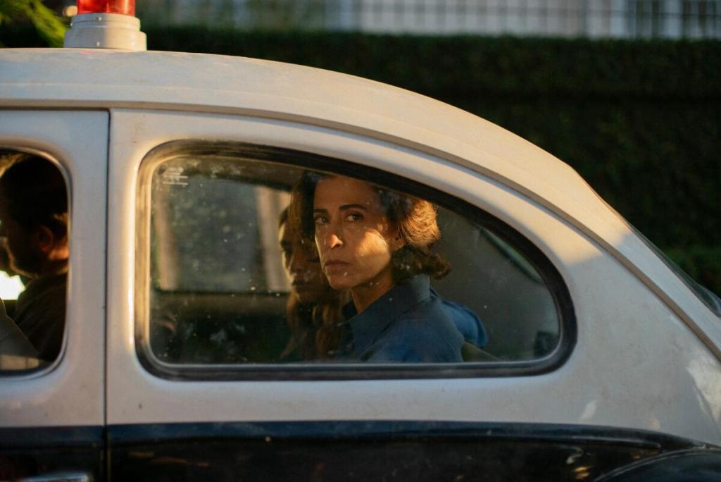 Brazilian actress Fernanda Torres
as Eunice Paiva in the back of a police car looking solemnly towards camera.