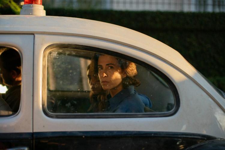 Brazilian actress Fernanda Torres as Eunice Paiva in the back of a police car looking solemnly towards camera.