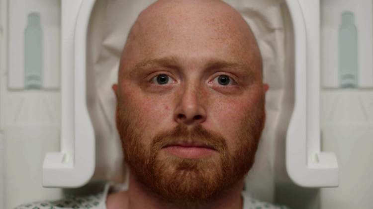 Close up of a man staring directly into camera while lying in an MRI machine