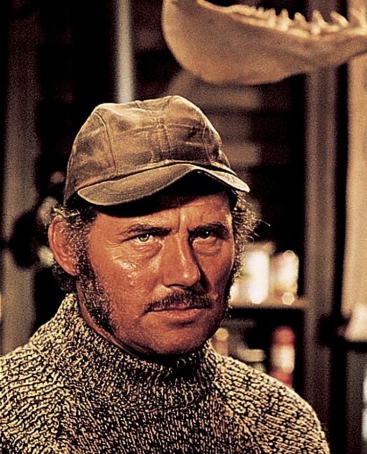 Close-up of Quint, the shark hunter from Jaws, with a weathered face, wearing a baseball cap, and looking intensely at something off-camera